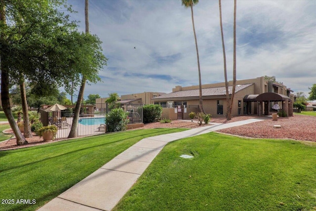 view of front of home with a community pool, stucco siding, fence, and a front lawn