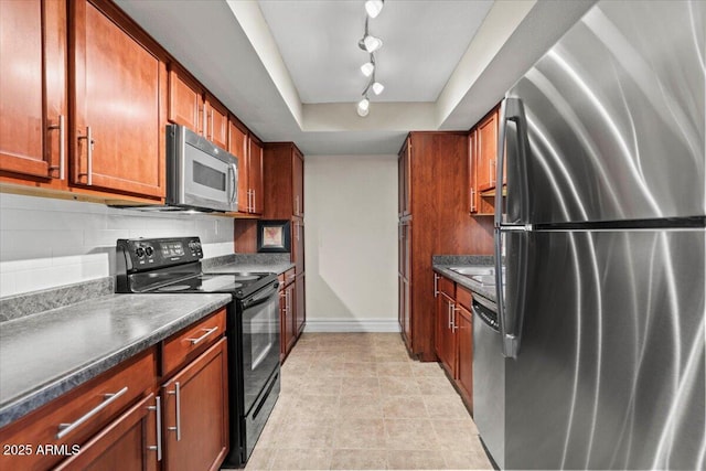 kitchen featuring dark countertops, track lighting, stainless steel appliances, baseboards, and a tray ceiling