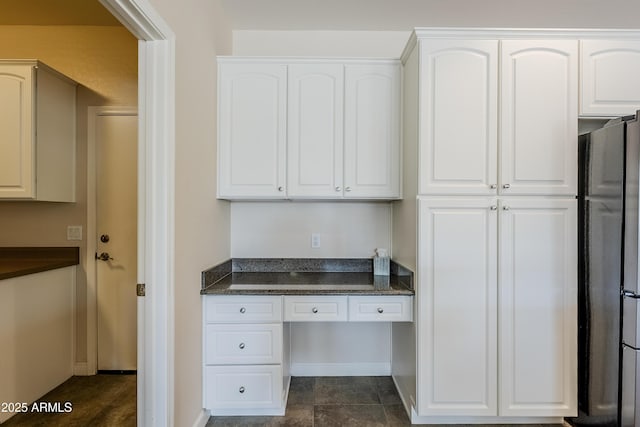 kitchen featuring dark stone counters, built in desk, stainless steel refrigerator, and white cabinets