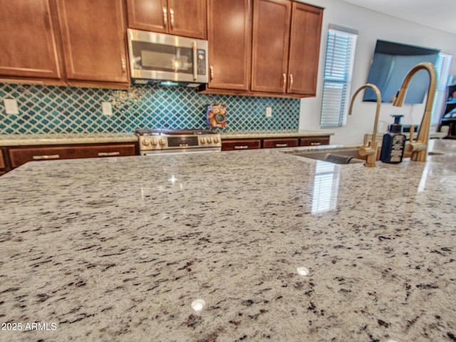 15817 S 177th Dr, Goodyear, AZ 85338 - kitchen with appliances with stainless steel finishes, a sink, light stone countertops, tasteful backsplash, and brown cabinetry