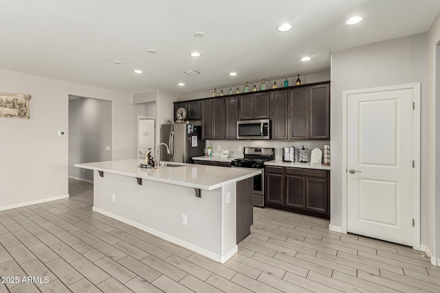 12357 W Whyman Ave, Avondale, AZ 85323 - kitchen featuring appliances with stainless steel finishes, an island with sink, dark brown cabinets, a kitchen breakfast bar, and recessed lighting