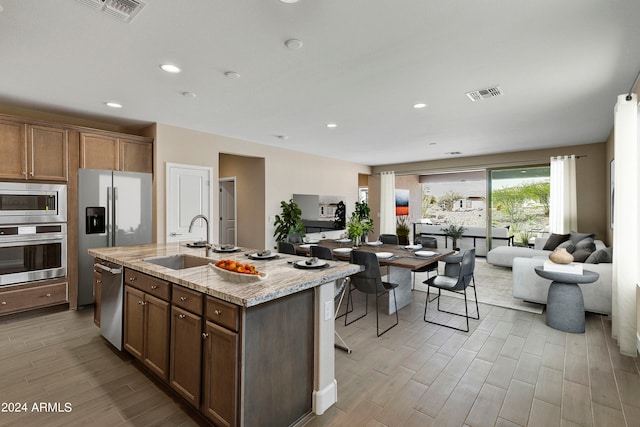 kitchen featuring sink, a kitchen island with sink, stainless steel appliances, light stone countertops, and light hardwood / wood-style floors