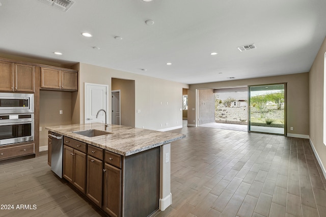 kitchen featuring sink, a kitchen island with sink, light hardwood / wood-style flooring, appliances with stainless steel finishes, and light stone countertops