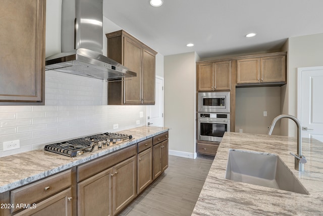 kitchen with wall chimney range hood, light hardwood / wood-style flooring, sink, stainless steel appliances, and light stone countertops