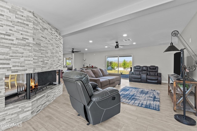 living room with beamed ceiling, ceiling fan, a stone fireplace, and light hardwood / wood-style flooring