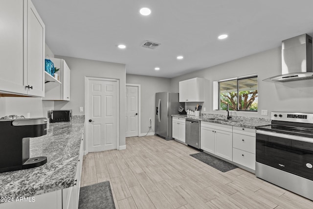 kitchen with white cabinets, wall chimney range hood, sink, light hardwood / wood-style flooring, and stainless steel appliances