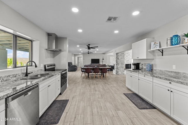 kitchen with sink, wall chimney exhaust hood, appliances with stainless steel finishes, light stone counters, and white cabinetry