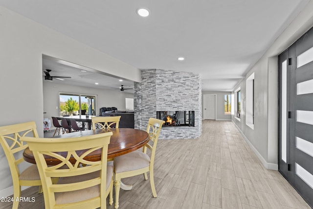 dining space featuring light hardwood / wood-style floors, a stone fireplace, and ceiling fan