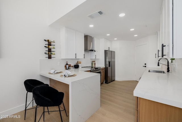 7710 E Gainey Ranch Rd E Unit 115, Scottsdale, AZ 85258 - kitchen featuring wall chimney exhaust hood, stainless steel refrigerator with ice dispenser, a peninsula, light stone countertops, and recessed lighting