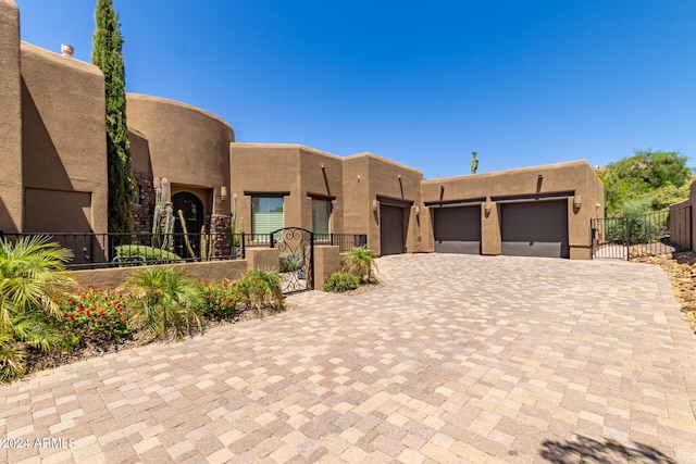 pueblo-style house featuring decorative driveway, an attached garage, fence, and stucco siding