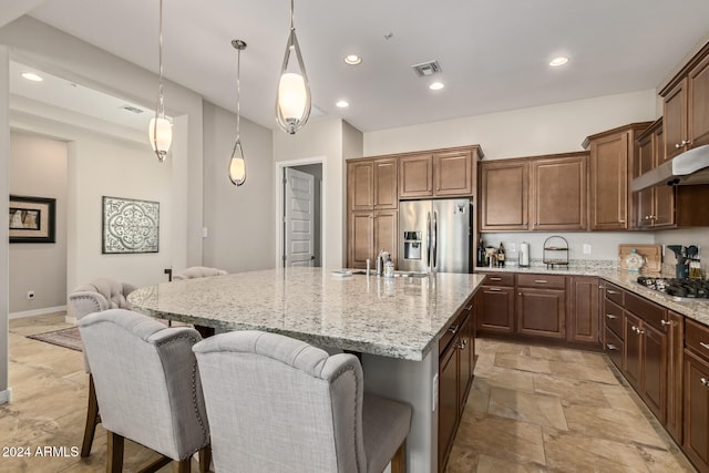 kitchen with light stone countertops, sink, hanging light fixtures, a center island with sink, and appliances with stainless steel finishes