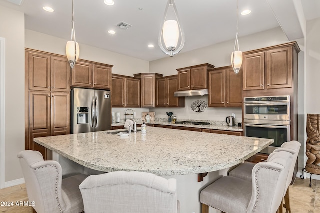 kitchen with a kitchen bar, appliances with stainless steel finishes, sink, decorative light fixtures, and an island with sink