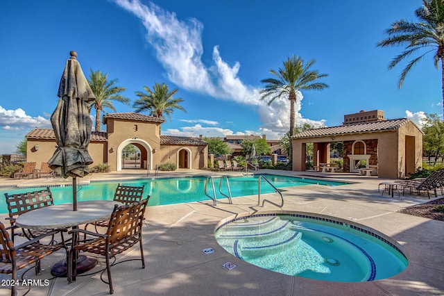 view of swimming pool featuring exterior fireplace, a patio, and a hot tub