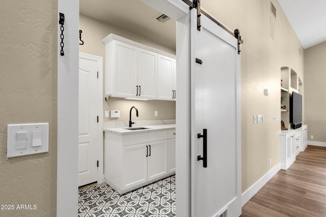 bar featuring visible vents, light wood-style flooring, a sink, a barn door, and baseboards