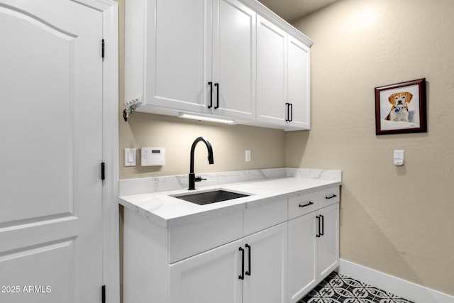 kitchen with light stone countertops, baseboards, a sink, white cabinets, and a textured wall