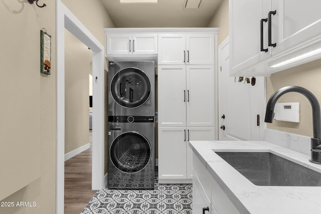 laundry room featuring cabinet space, stacked washing maching and dryer, light wood-style floors, and a sink