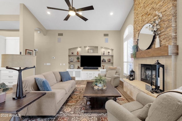 living room with visible vents, high vaulted ceiling, wood finished floors, and a tiled fireplace