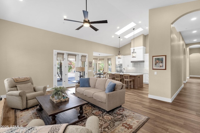 living room featuring ceiling fan, baseboards, wood finished floors, arched walkways, and high vaulted ceiling