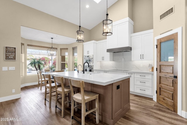 kitchen featuring wood finished floors, backsplash, an island with sink, and white cabinetry