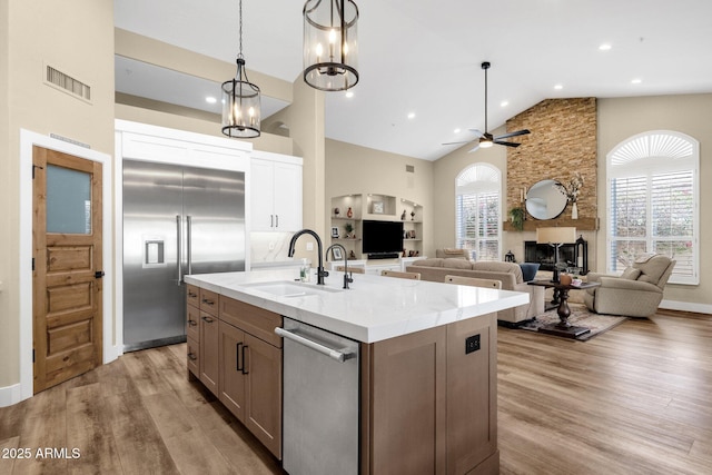 kitchen featuring visible vents, a sink, a large fireplace, light wood-style floors, and appliances with stainless steel finishes