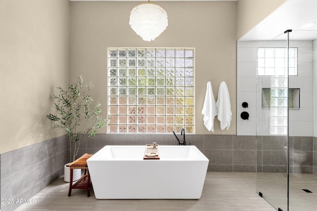 bathroom with a chandelier, a tile shower, wainscoting, a freestanding tub, and tile walls