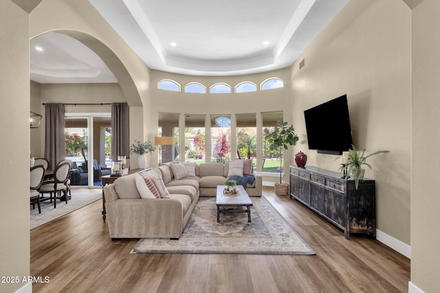 living area featuring visible vents, a tray ceiling, wood finished floors, baseboards, and a towering ceiling