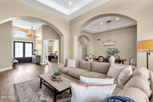 living room with wood finished floors, baseboards, a tray ceiling, french doors, and a chandelier