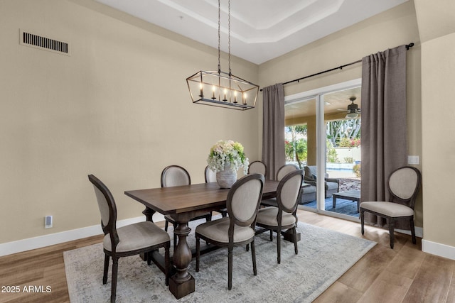 dining room featuring visible vents, baseboards, light wood-type flooring, ceiling fan with notable chandelier, and a raised ceiling