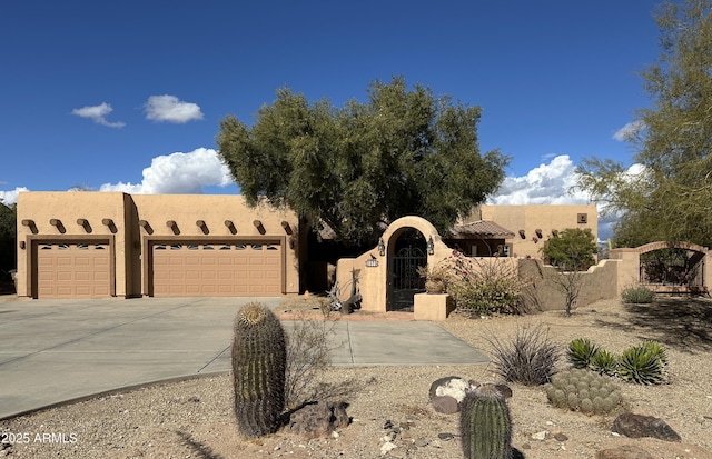 adobe home featuring a fenced front yard, stucco siding, concrete driveway, an attached garage, and a gate