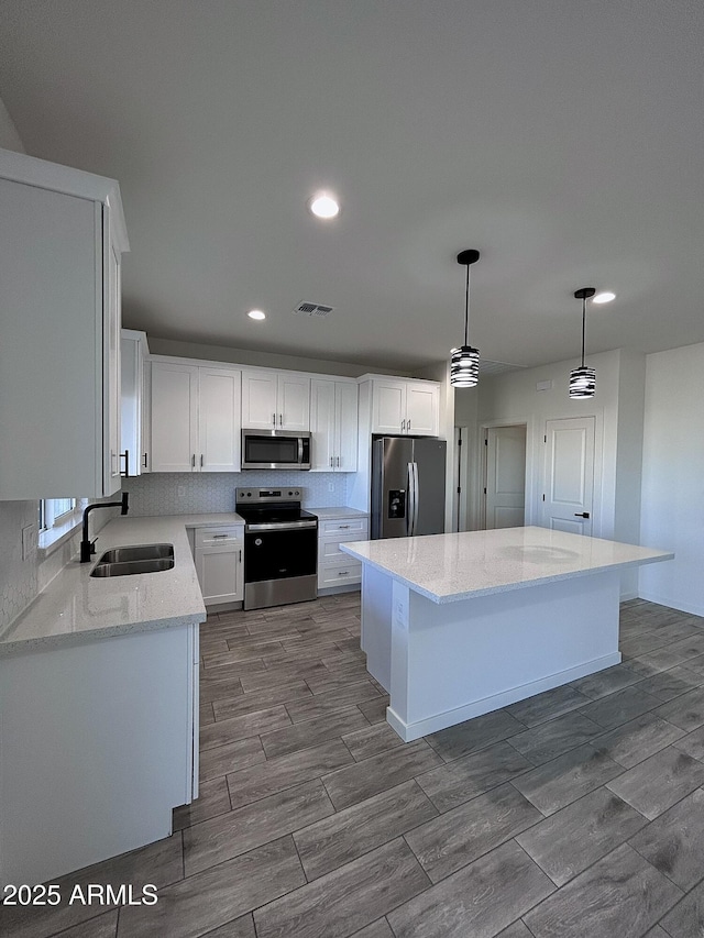 kitchen with sink, a kitchen island, decorative light fixtures, white cabinets, and appliances with stainless steel finishes