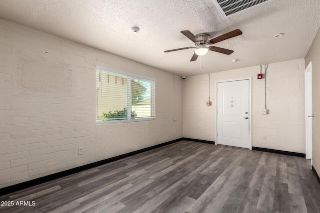 unfurnished room featuring a textured ceiling, brick wall, wood finished floors, visible vents, and a ceiling fan