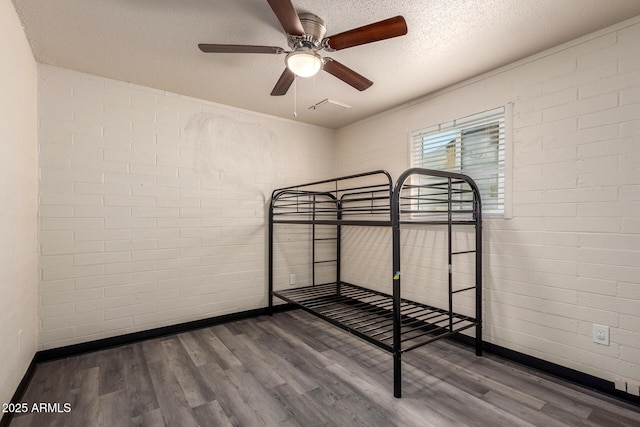 unfurnished bedroom with baseboards, a textured ceiling, brick wall, and wood finished floors