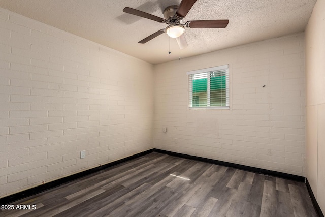 spare room featuring a textured ceiling, brick wall, dark wood-style flooring, and baseboards