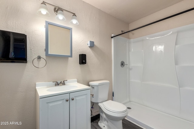 full bath featuring toilet, a shower, a textured wall, and vanity