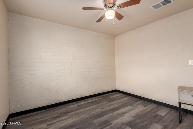 spare room featuring visible vents, ceiling fan, brick wall, wood finished floors, and baseboards