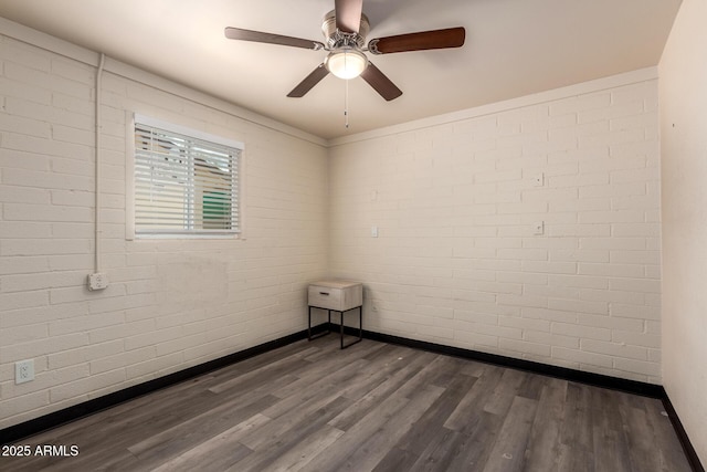 empty room featuring brick wall, dark wood-style flooring, and baseboards