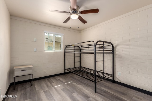 bedroom with baseboards, ceiling fan, brick wall, and wood finished floors