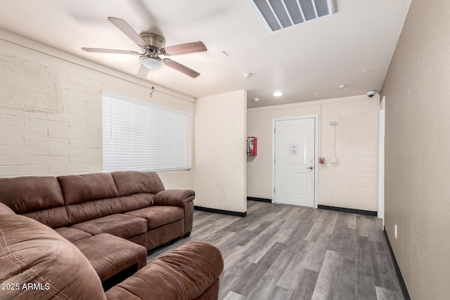 living area featuring brick wall, wood finished floors, visible vents, baseboards, and a ceiling fan