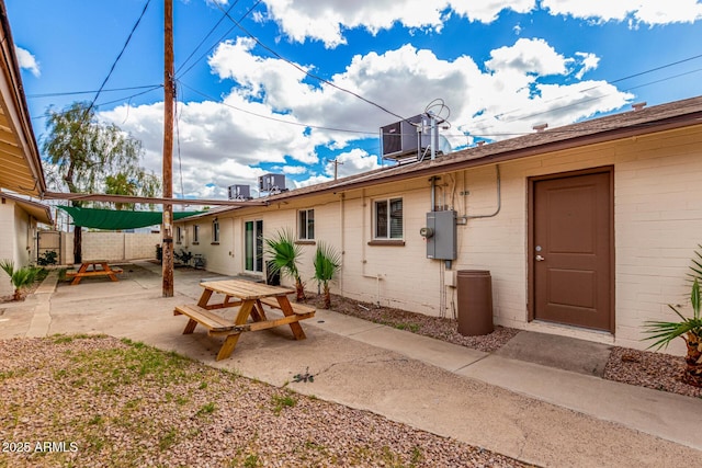 rear view of property featuring a patio area, central AC, brick siding, and fence