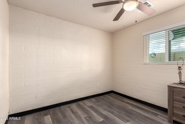 spare room featuring a textured ceiling, brick wall, dark wood finished floors, and visible vents