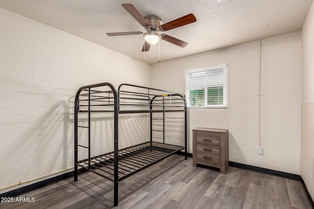 unfurnished bedroom featuring a textured ceiling, brick wall, and wood finished floors