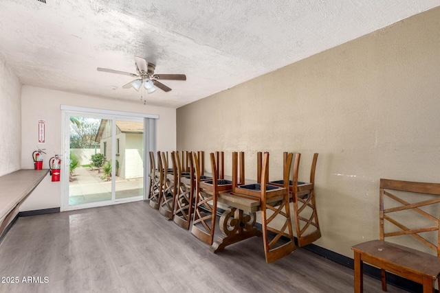 dining space with ceiling fan, a textured wall, a textured ceiling, and wood finished floors