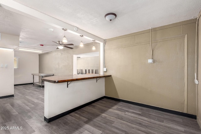 kitchen featuring butcher block counters, hanging light fixtures, dark wood-type flooring, a peninsula, and baseboards