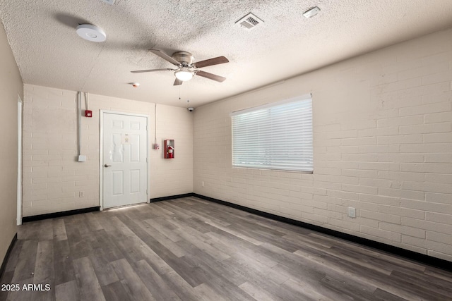 unfurnished room featuring visible vents, ceiling fan, a textured ceiling, brick wall, and wood finished floors