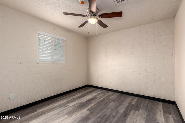 empty room featuring a textured ceiling, brick wall, dark wood-type flooring, and visible vents