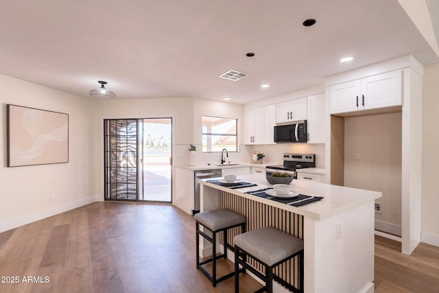 kitchen with a sink, wood finished floors, visible vents, baseboards, and appliances with stainless steel finishes