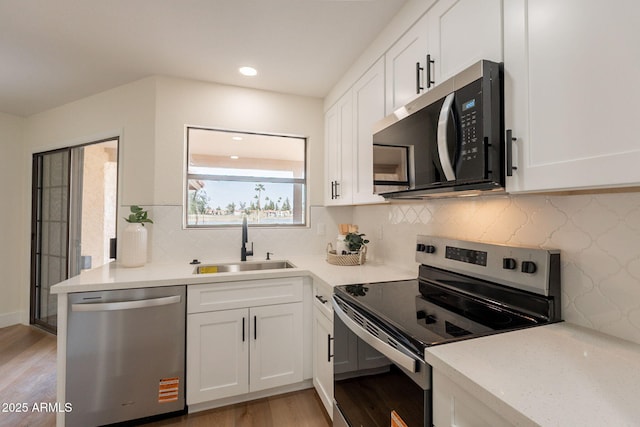 kitchen with stainless steel appliances, light wood finished floors, a sink, white cabinetry, and light countertops