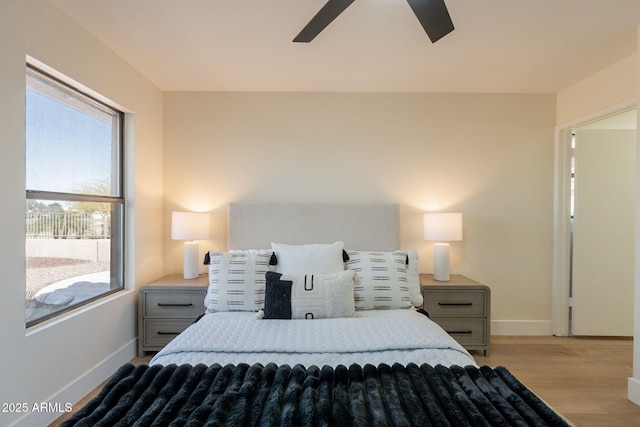 bedroom featuring baseboards, multiple windows, a ceiling fan, and wood finished floors