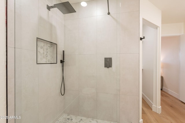 bathroom featuring baseboards, wood finished floors, and tiled shower