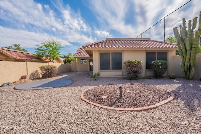 back of house featuring stucco siding, a tile roof, and fence